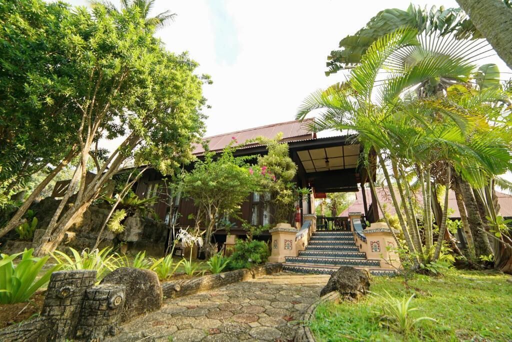 A traditional building with a covered entrance, stone steps, and lush tropical vegetation.