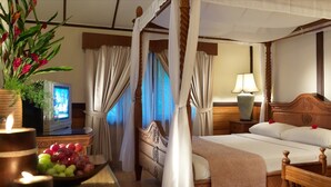 A four-poster canopy bed with a wooden headboard, a bedside table with a lamp, and a television on a stand. - Lavilla By Holiday Villa Cherating (Cherating)