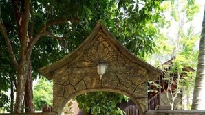 A stone archway leading to a garden area with various plants and a wooden structure in the background. - Lavilla By Holiday Villa Cherating (Cherating)