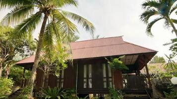 A wooden house with a sloped roof, surrounded by palm trees and greenery.