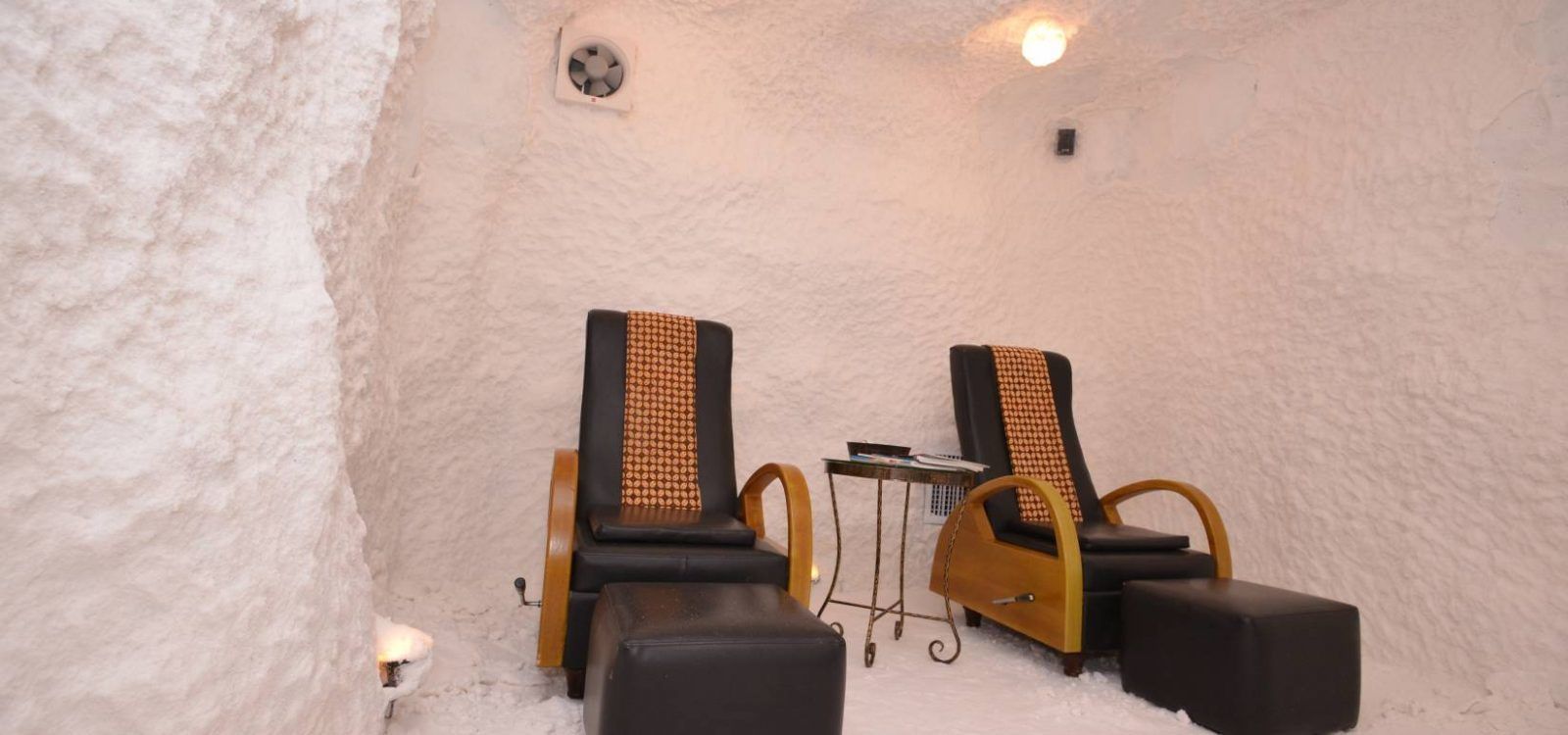 A sauna room with two black chairs with wooden armrests and a small table.