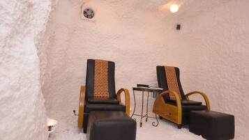 A sauna room with two black chairs with wooden armrests and a small table.