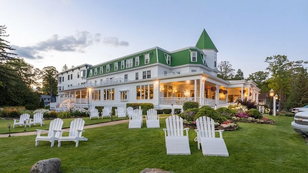 A large, multi-story building with a green roof and white walls, surrounded by a well-maintained lawn and Adirondack chairs. - Bay View Inn (Petoskey)