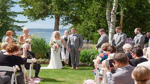 A wedding ceremony outdoors with guests seated on chairs facing the couple. - Bay View Inn (Petoskey)