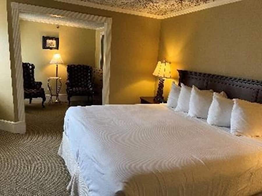 Habitación de hotel con una cama grande, una mesita de noche con lámpara y una silla en la esquina.