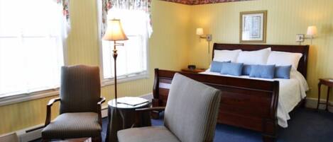 Een hotelkamer met een bed, twee stoelen, een kleine tafel en een lamp.