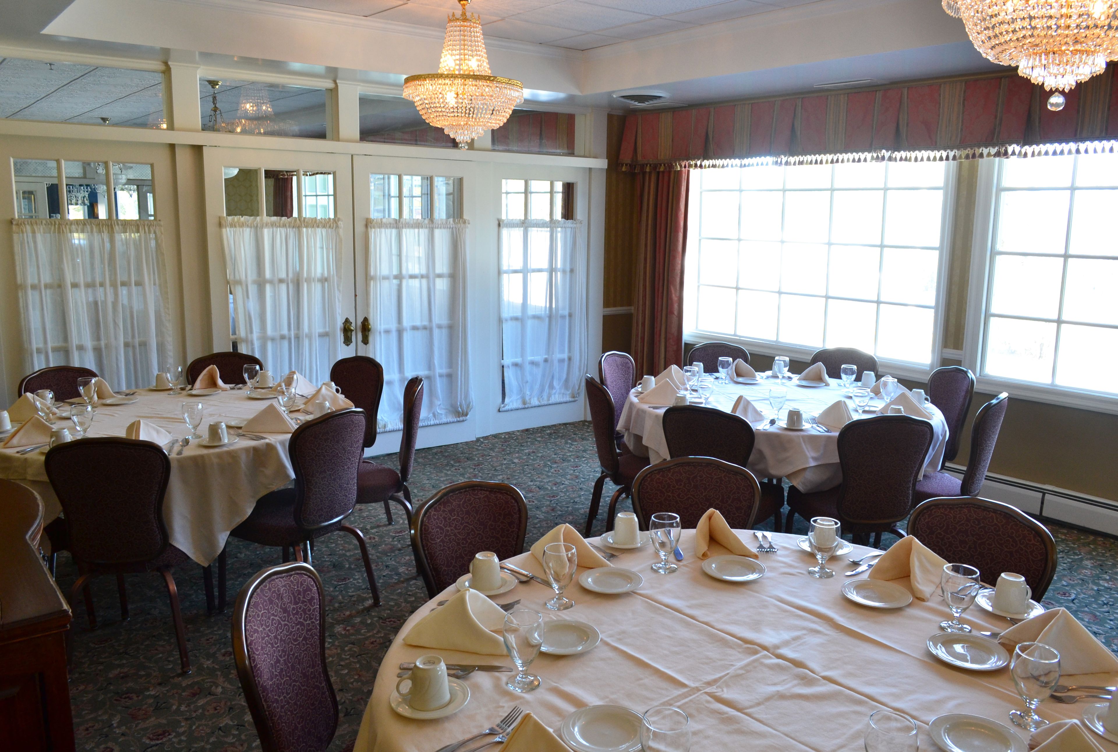 A dining area with tables set for a meal, chairs, and chandeliers.
