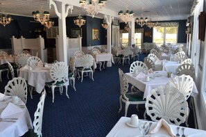 A dining area with white chairs, tables, and chandeliers.