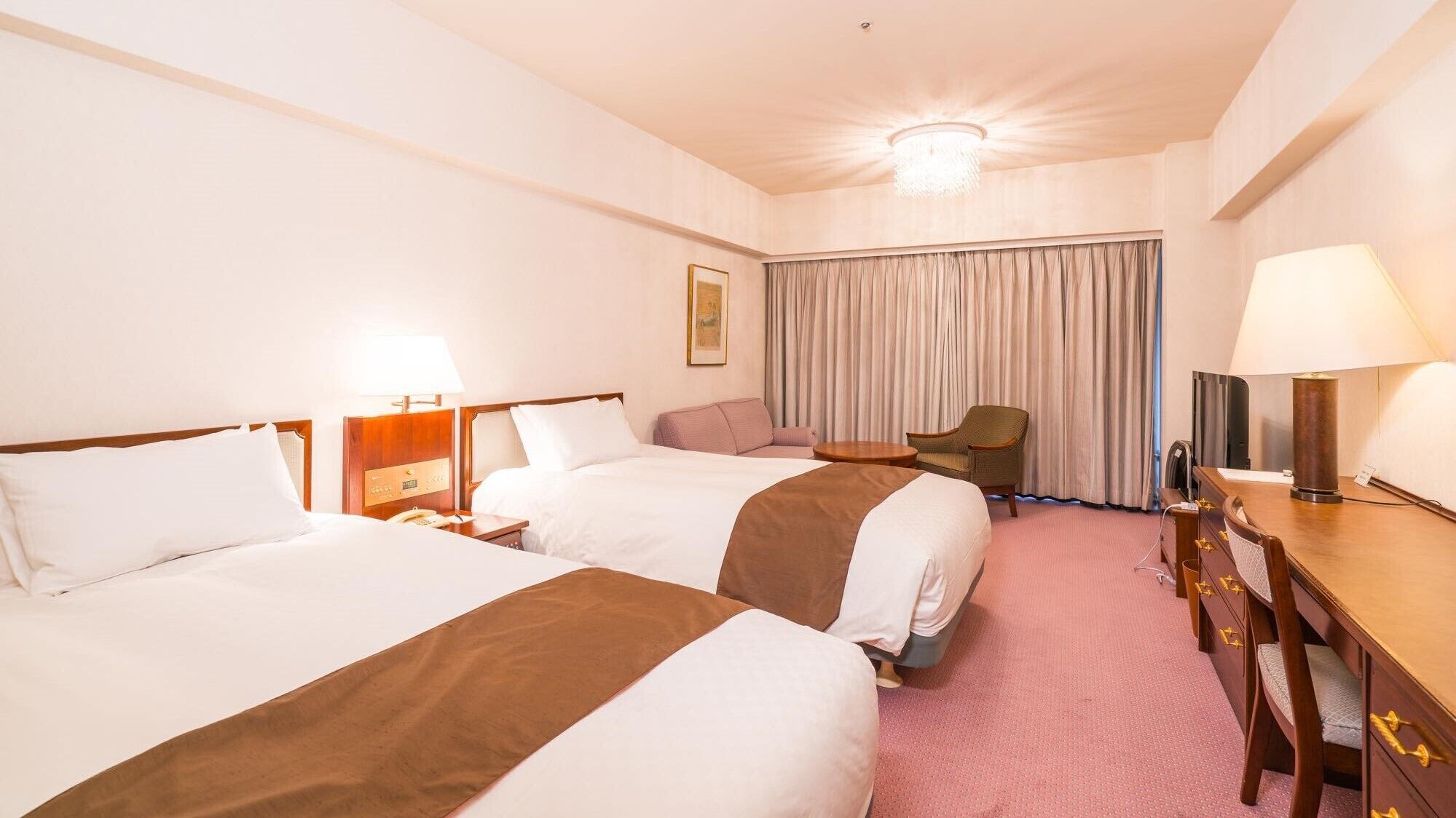A hotel room with two beds, a desk, a chair, a television, and a large window with curtains.