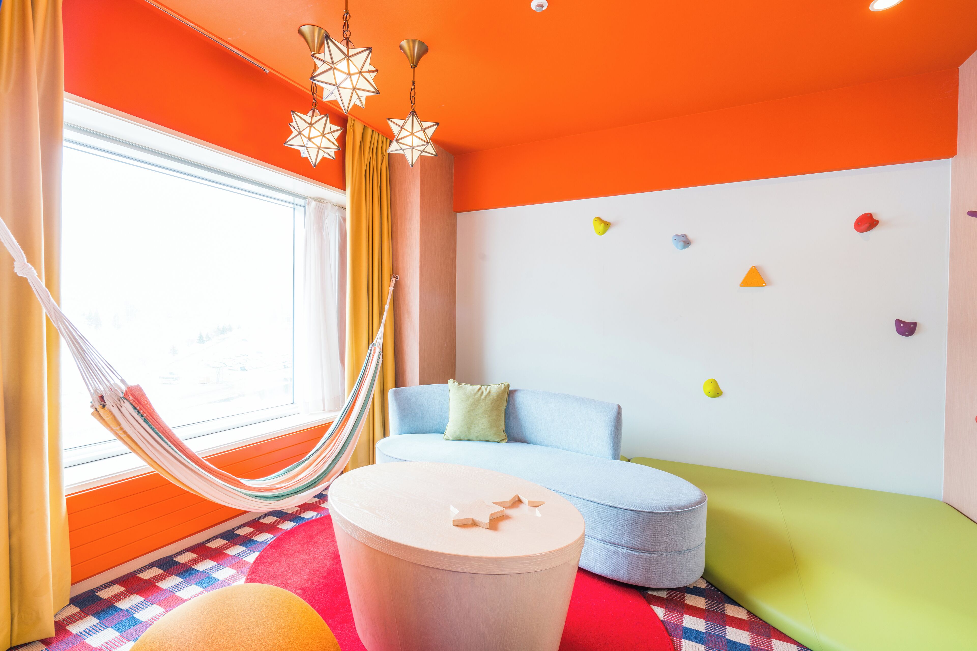 A room with a hammock, a round table, a sofa, and colorful wall decorations.