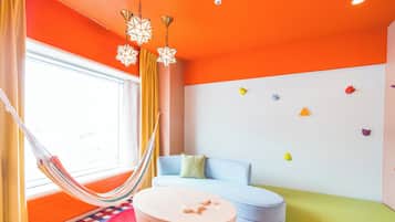 A room with a hammock, a round table, a sofa, and colorful wall decorations.