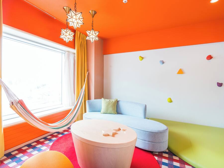 A room with a hammock, a round table, a sofa, and colorful wall decorations.