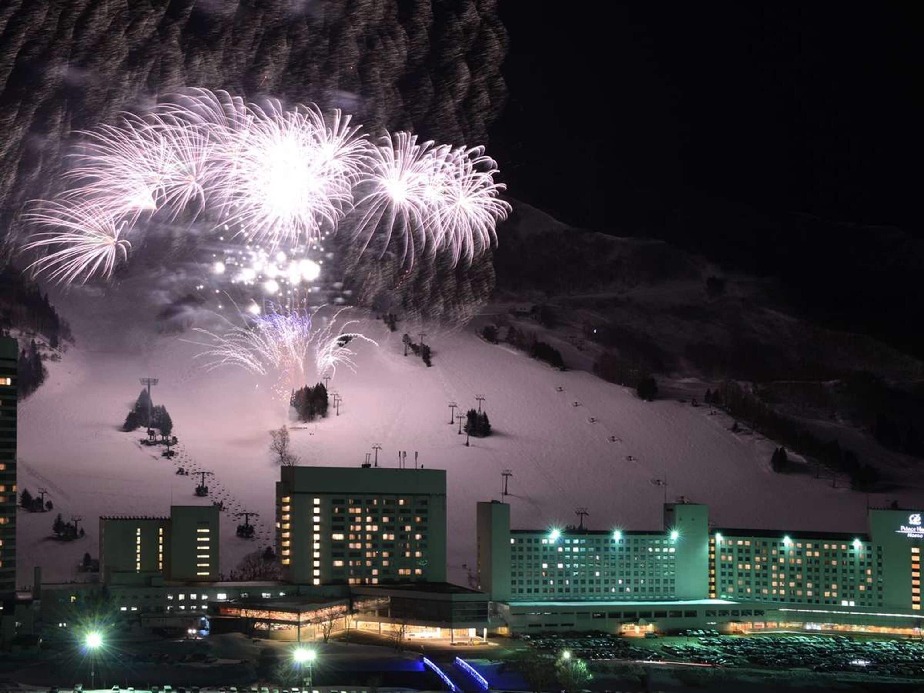 Um hotel com vários edifícios, pistas de esqui ao fundo e fogos de artifício.