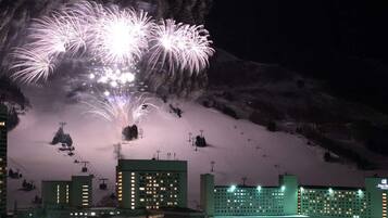 Um hotel com vários edifícios, pistas de esqui ao fundo e fogos de artifício.