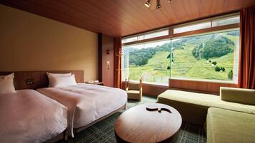 A hotel room with two beds, a sofa, a round table, and a large window offering a view of a green landscape.
