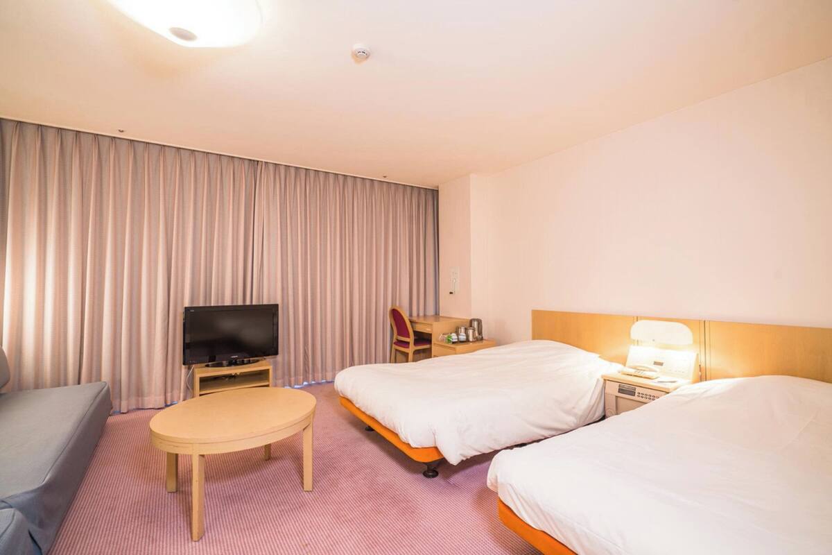 A hotel room with two beds, a television, a desk, and a chair.
