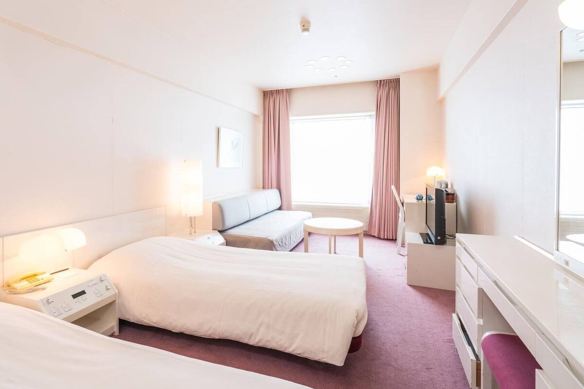 A hotel room with two beds, a desk, a chair, a TV, and a window with curtains.