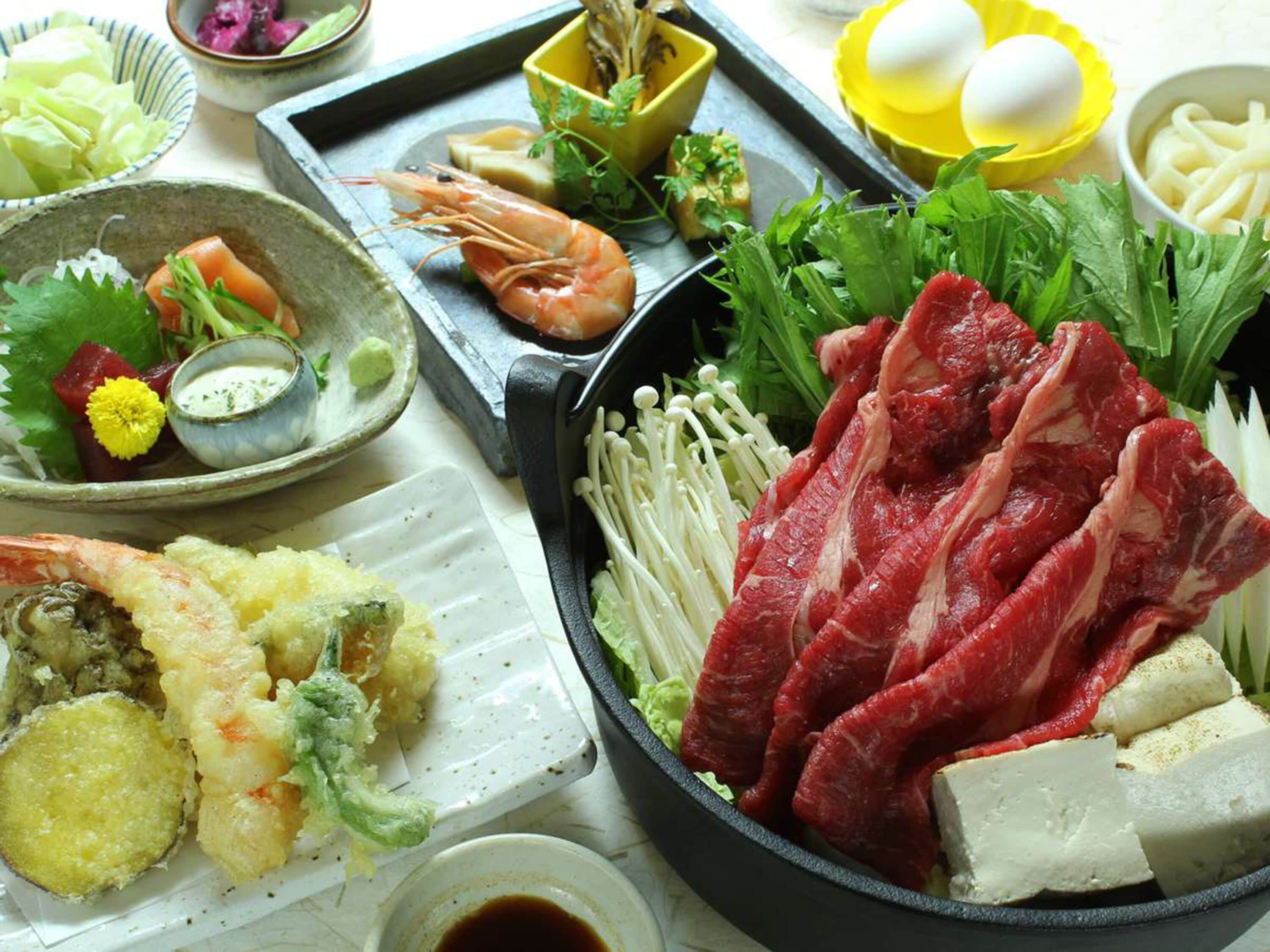 Variedad de platos japoneses, como sashimi, tempura y carne a la parrilla, presentados en una bandeja.