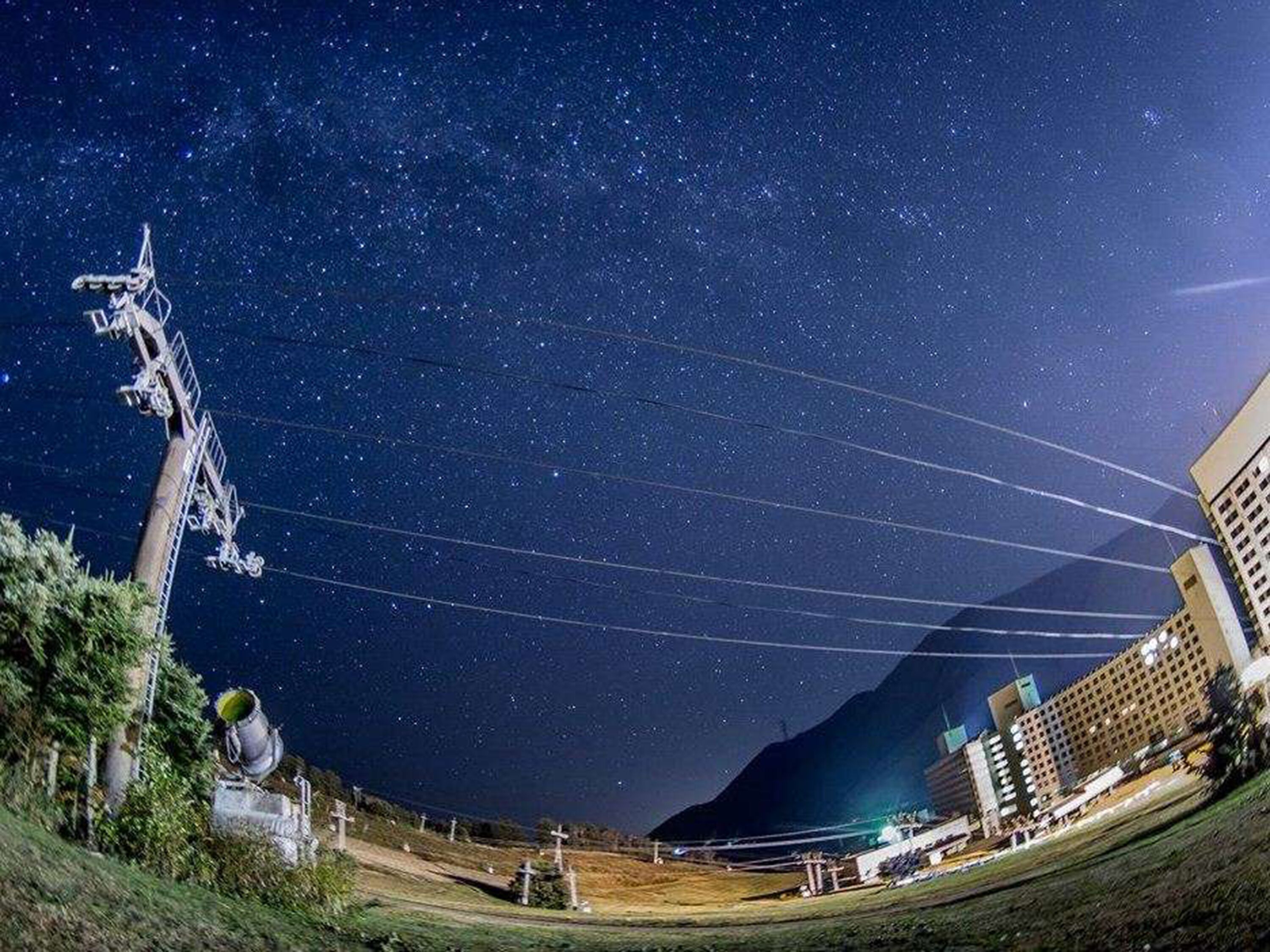 Vista nocturna de un paisaje urbano con cielo estrellado, líneas eléctricas y una montaña al fondo.