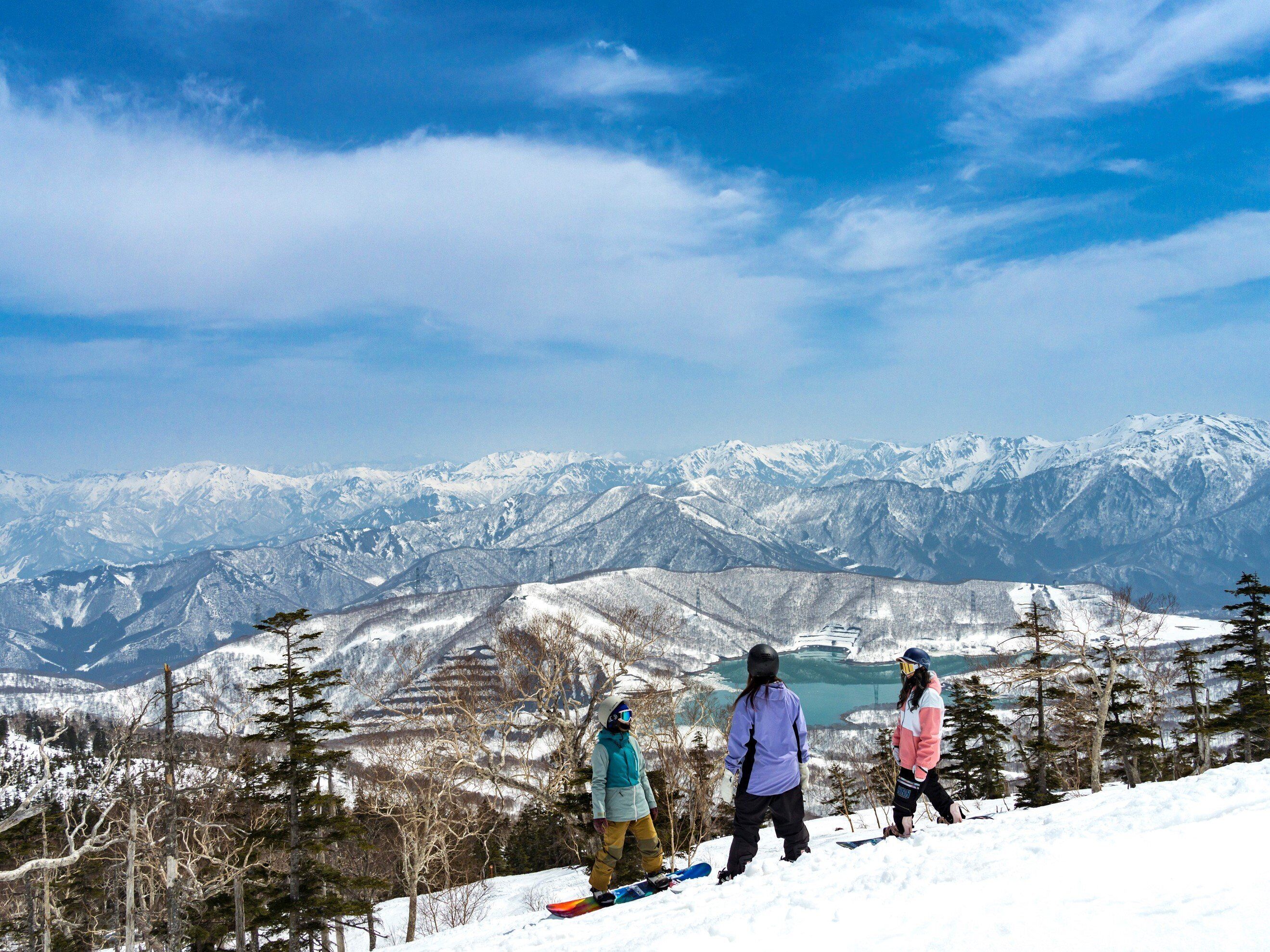 A snowy mountain landscape with three skiers and a snowboarder.