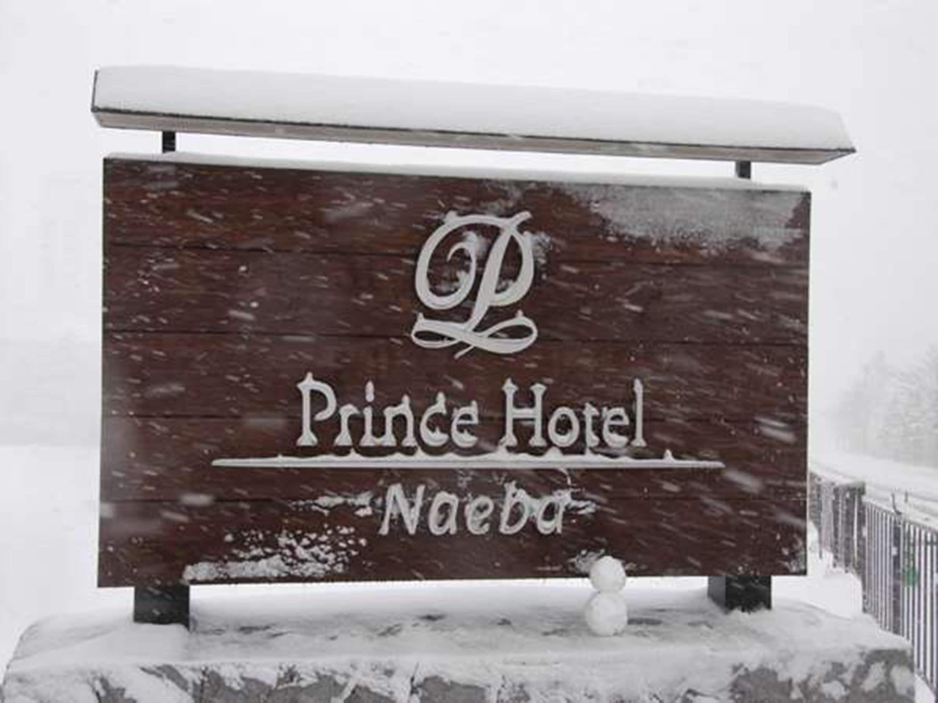 Señal de madera del Hotel Prince en Naebo, con un techo nevado y una figura de muñeco de nieve.