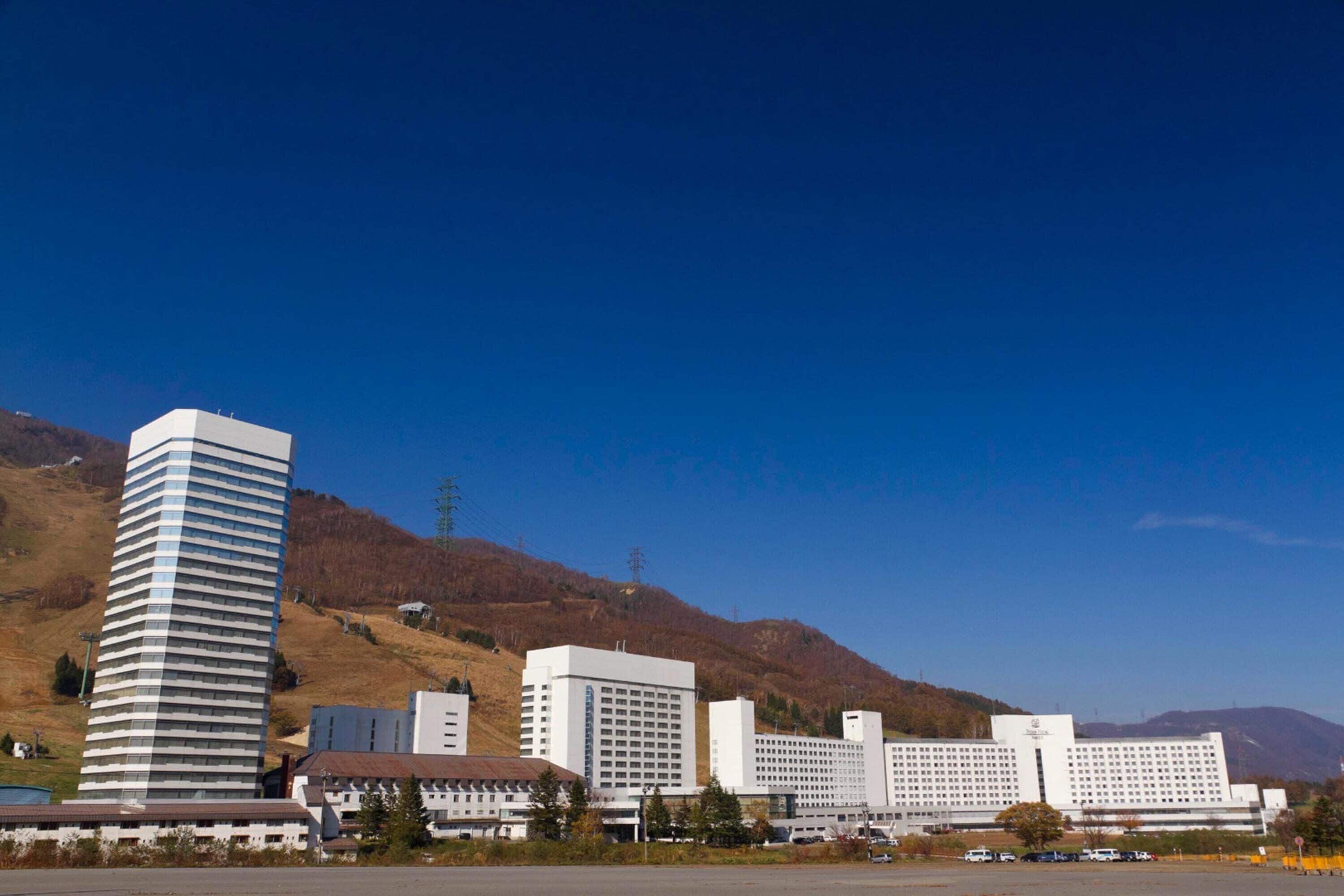 Un complejo hotelero moderno con varias edificaciones, incluyendo una estructura alta y cilíndrica y varios edificios rectangulares con techos planos.