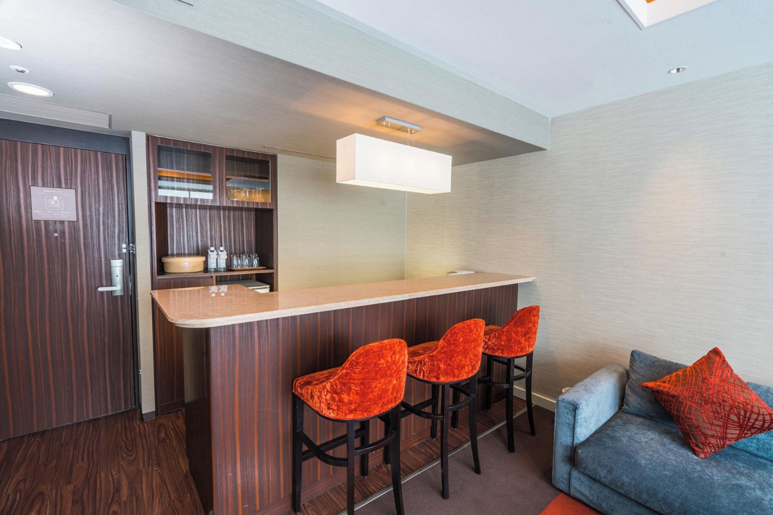 A modern kitchen with a bar area, wooden cabinets, and a blue sofa with a red pillow.