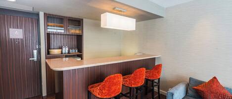A modern kitchen with a bar area, wooden cabinets, and a blue sofa with a red pillow.