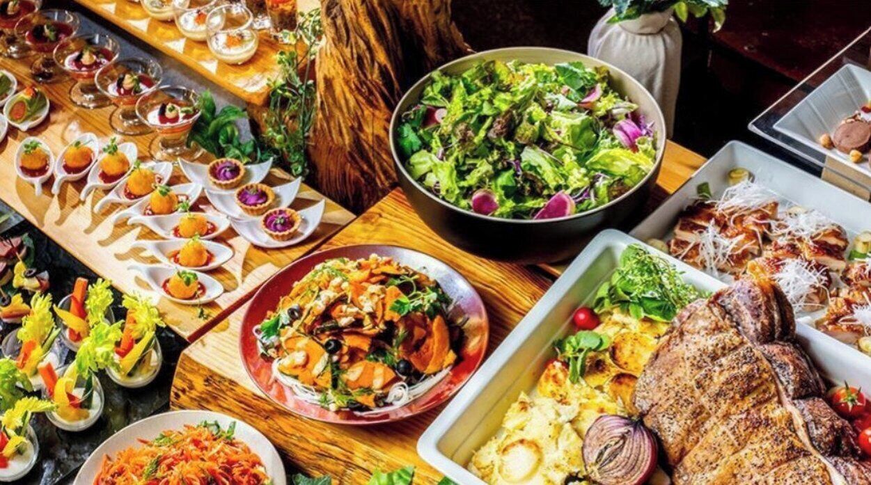 A variety of dishes and drinks on a wooden table, suggesting a buffet or communal dining setup.