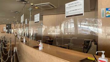 A hotel reception area with a counter, hand sanitizer, and a view of the outside through the glass.