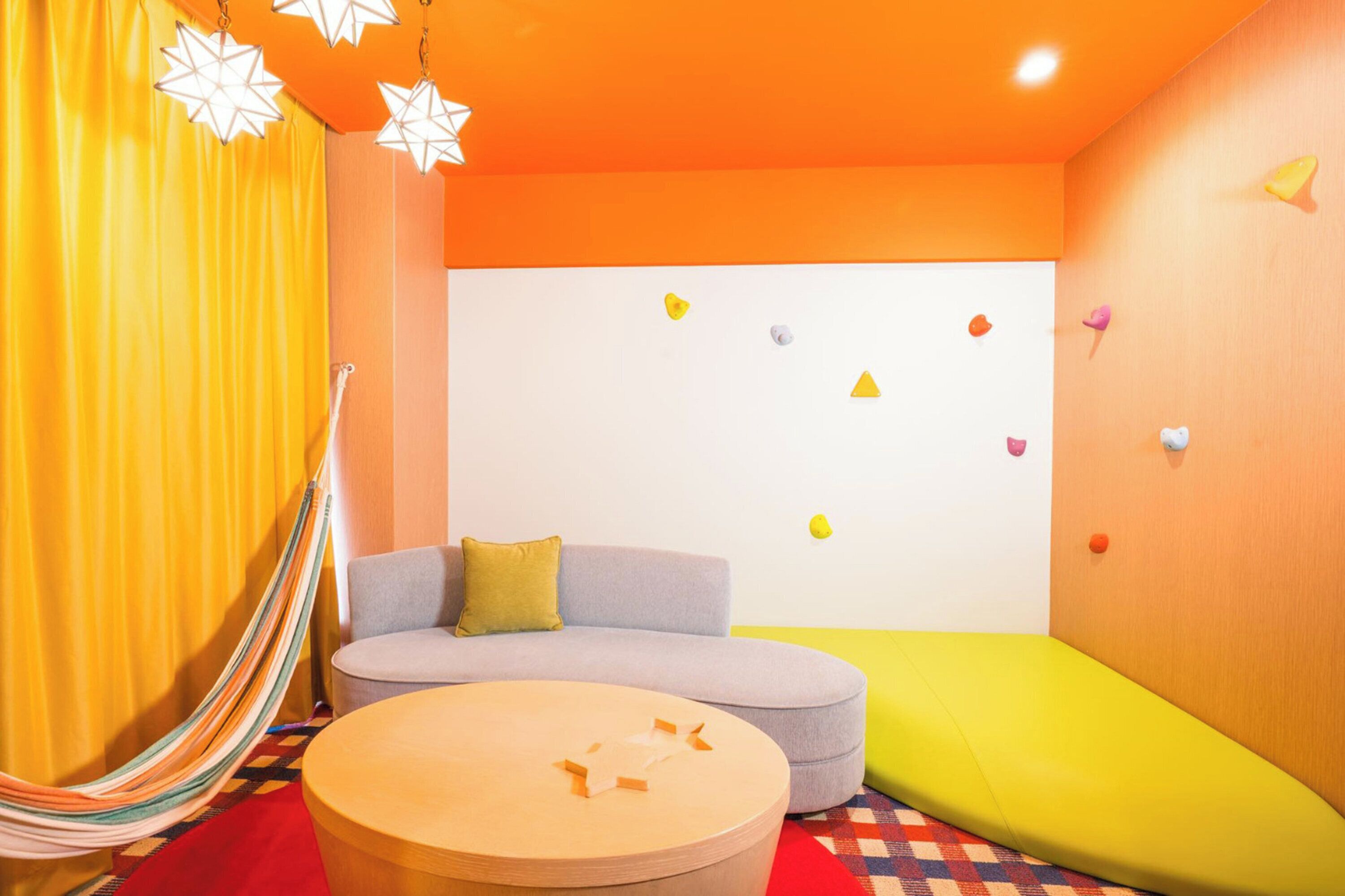 A room with a hammock, a round table, a sofa, and colorful wall decorations.