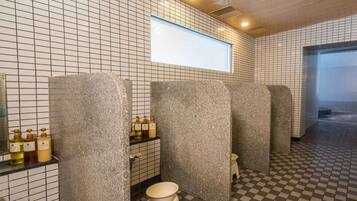 A public restroom with tiled walls and floors, granite pillars, and a checkered floor pattern.