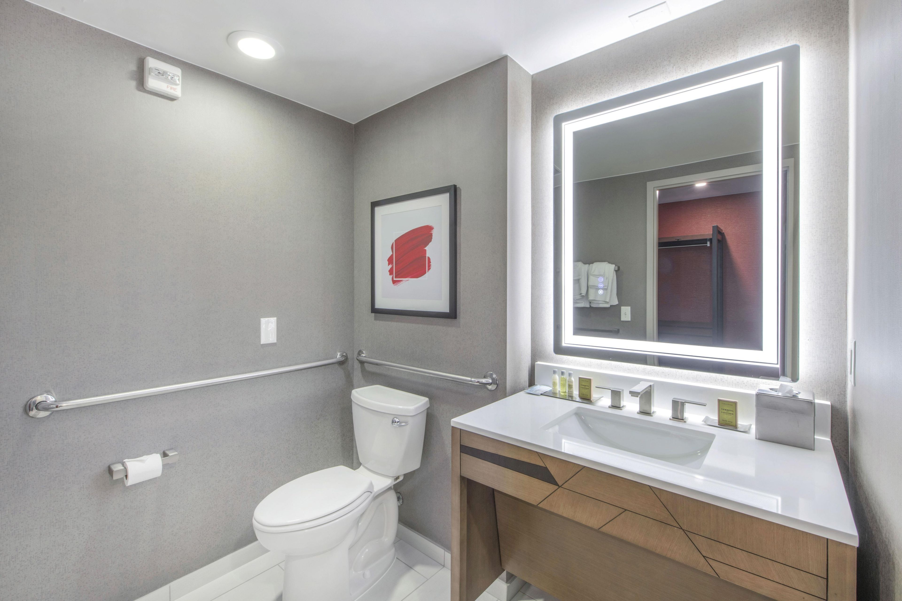 Un baño moderno con inodoro blanco, tocador con espejo y barra de apoyo.