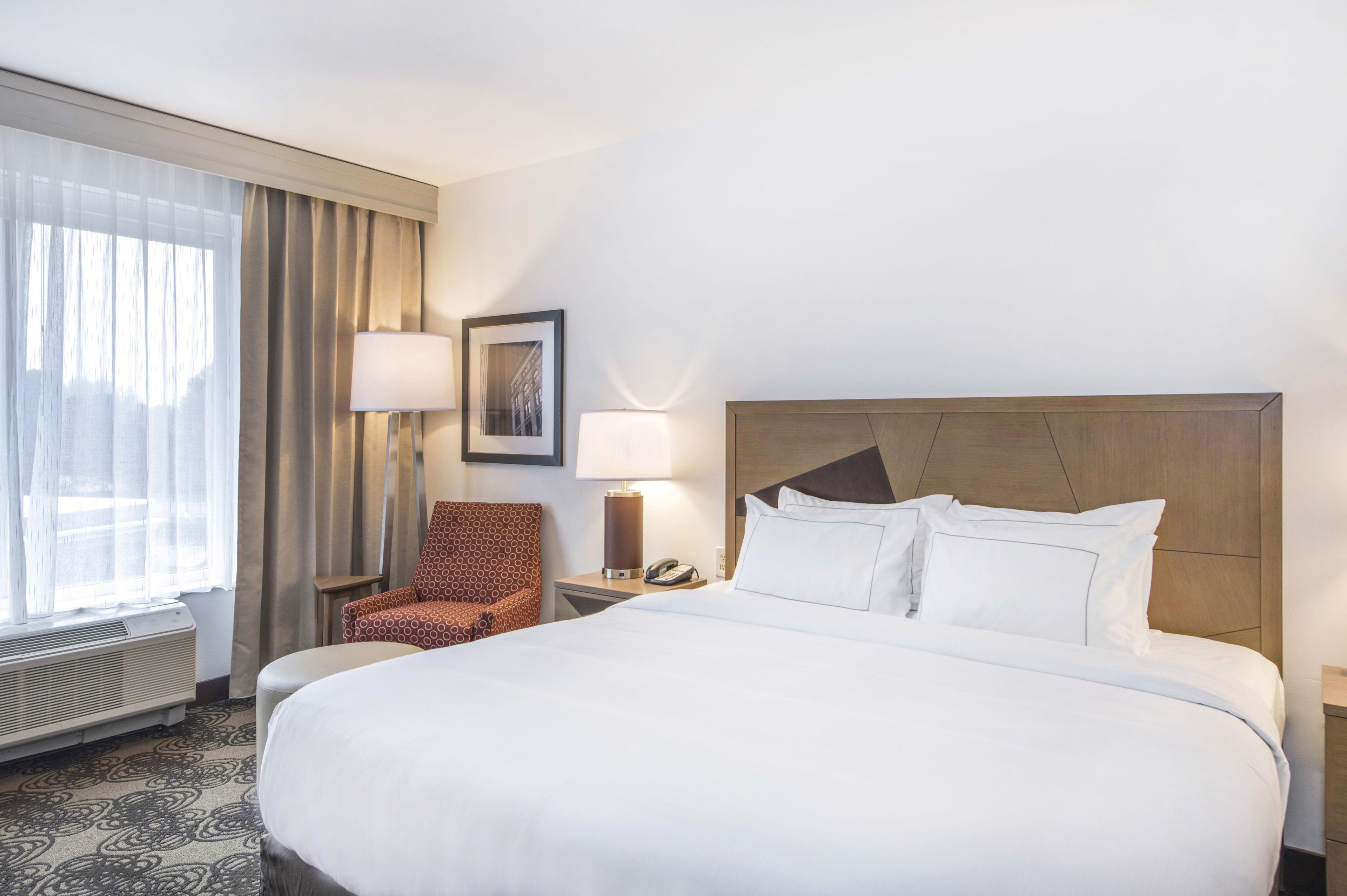A hotel room with a large bed, a chair, a desk with a lamp, and a picture on the wall.