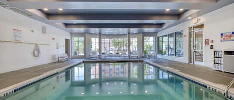 A clear indoor swimming pool with a tiled edge, a bench area, and a towel return station.