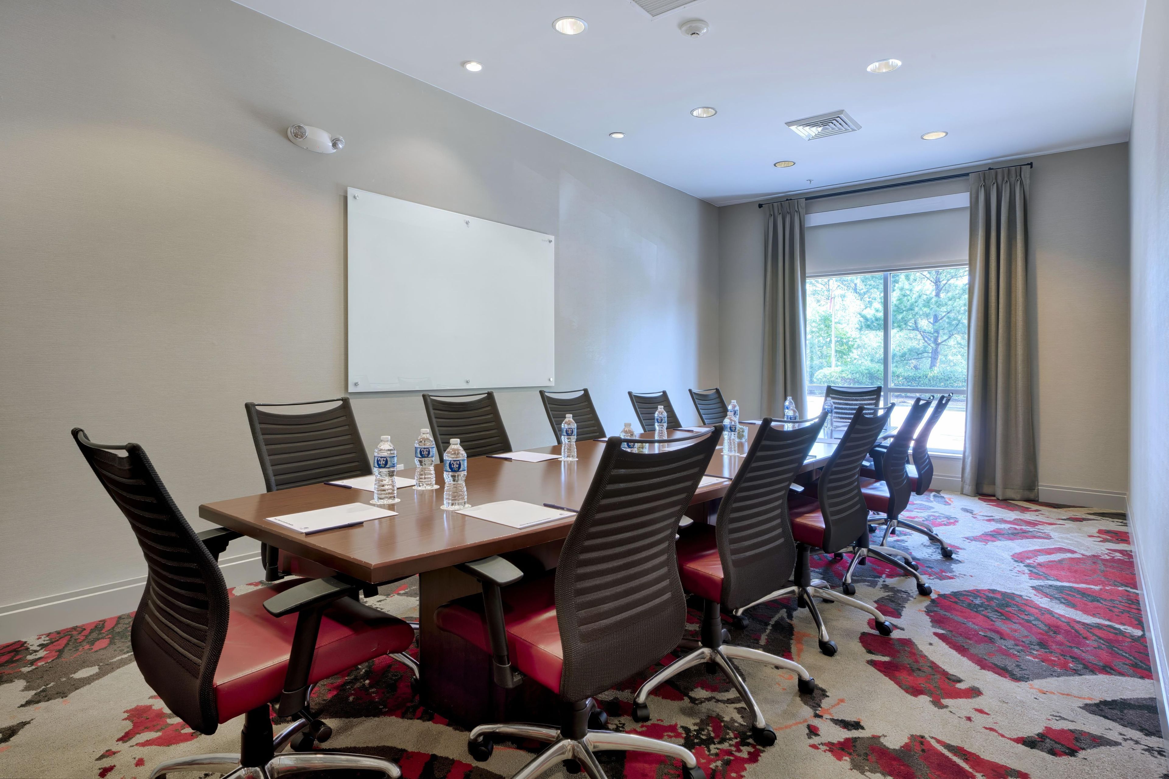 A conference room with a whiteboard, a long table with chairs, water bottles, and a carpeted floor.