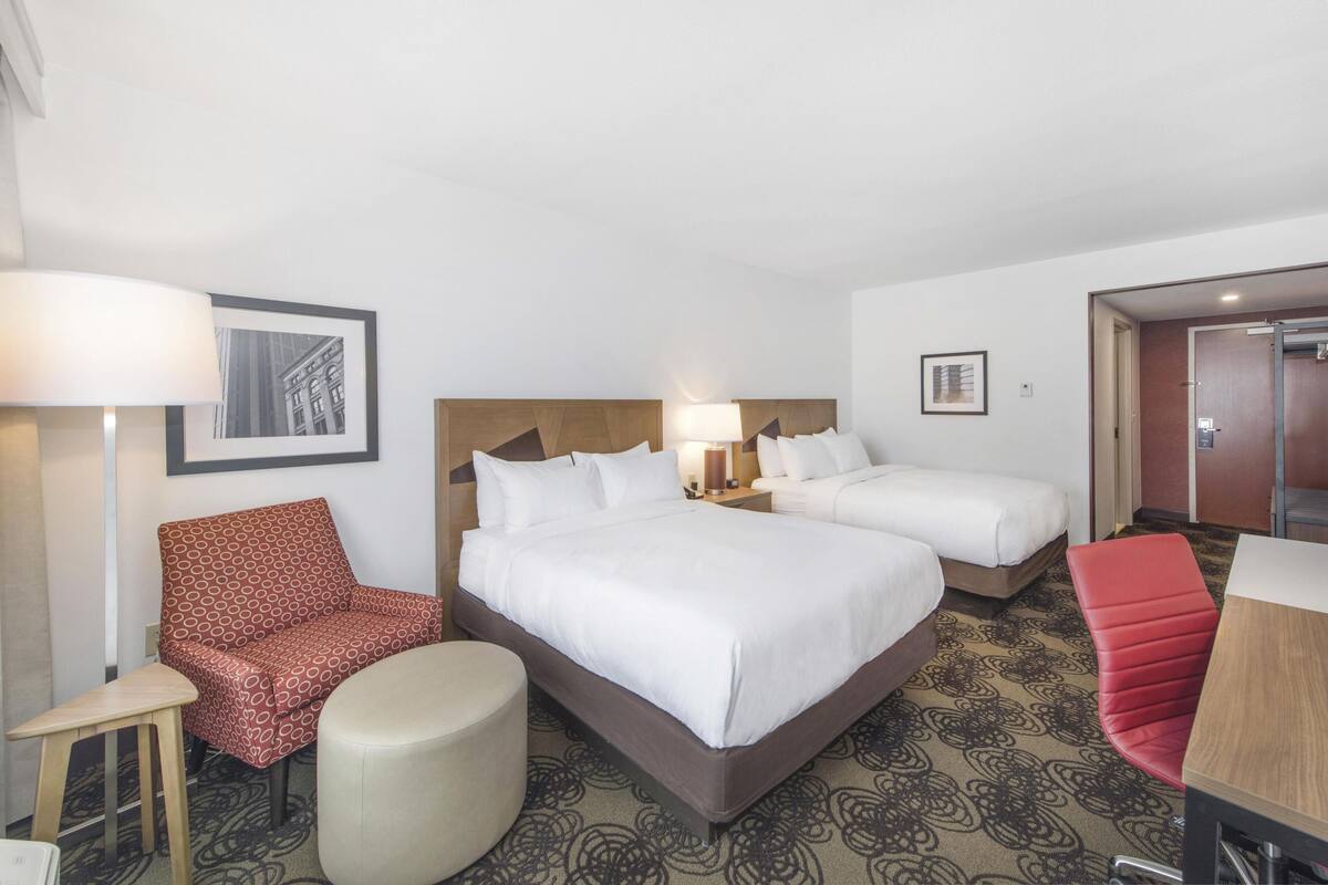 Habitación de hotel con dos camas, un escritorio, una silla y una lámpara.