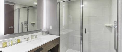 Une salle de bain moderne dotée d’une douche à parois de verre, d’un grand miroir et d’un meuble-lavabo avec un plan de travail blanc.