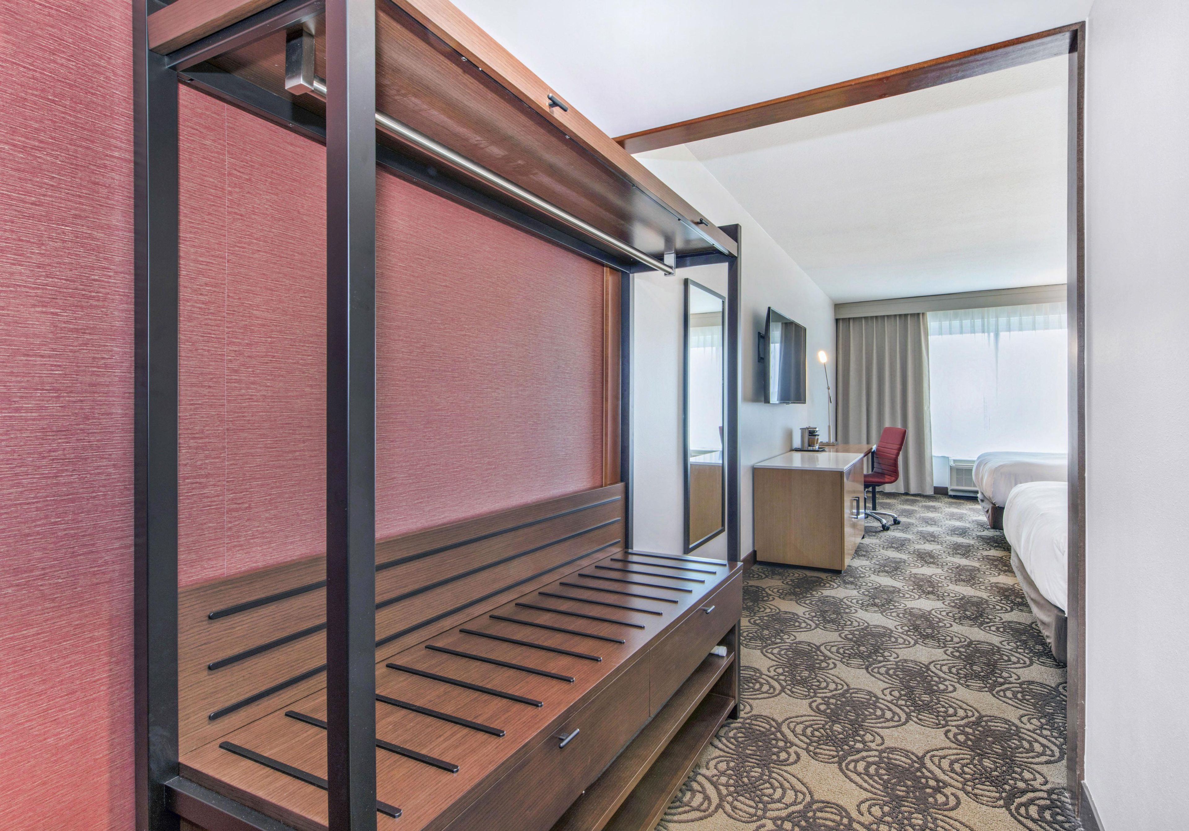 A hotel room with a bed, a desk, a chair, and a large mirror.