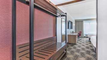 A hotel room with a bed, a desk, a chair, and a large mirror.