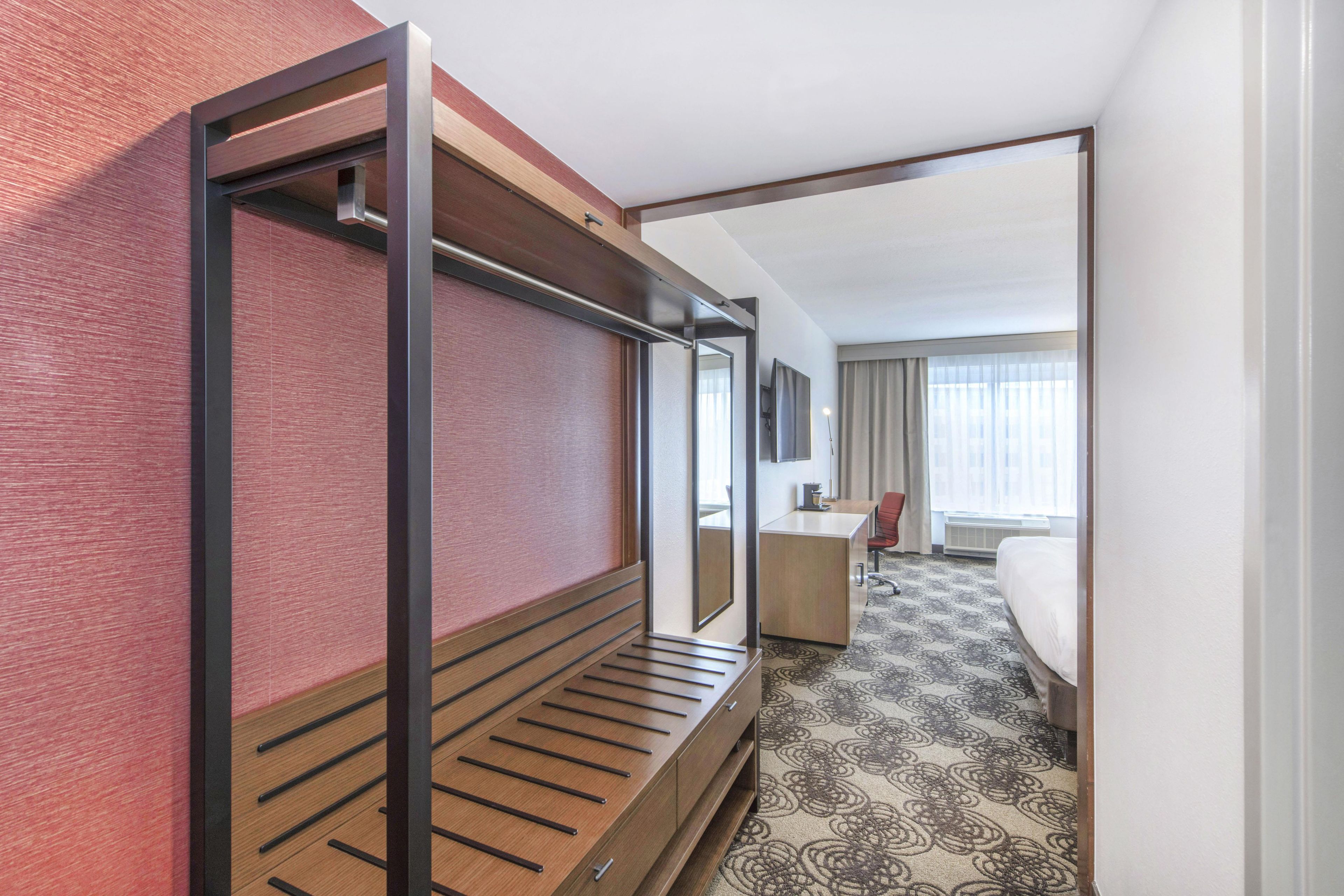 A hotel room with a bunk bed, a desk, a chair, a bed, and a patterned carpet.