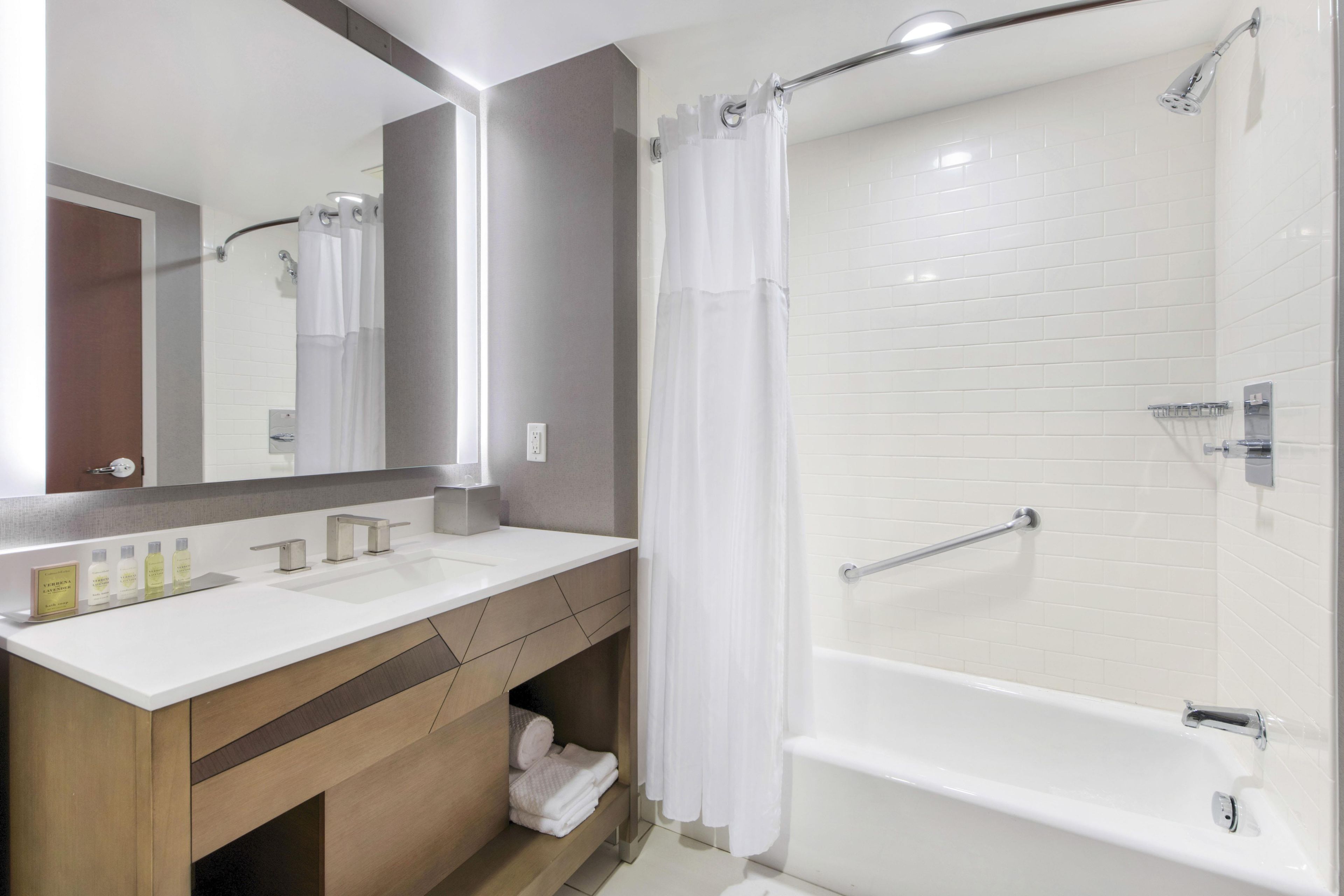 A modern bathroom with a white bathtub, a shower with a glass door, a vanity with a mirror, and a towel rack.