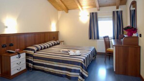A bedroom with a wooden bed, a desk, and a chair. - Hotel Bernina (Tirano)