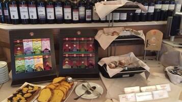 A hotel room with a minibar stocked with wine bottles, a selection of pastries, and a breakfast tray.