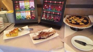 Una exposición de postres con varios pasteles y bollería, un panel con la carta y algunas fuentes con cubiertos.