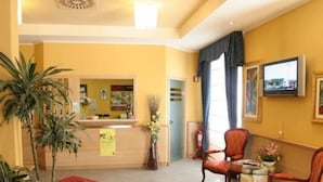 A hotel lobby with a reception desk, seating area, and a large window with curtains. - Hotel Bernina (Tirano)