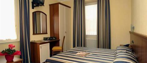 A hotel room with a bed, a desk, a chair, a TV, and a radiator.
