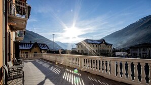 A terrace with a view of mountains, a building with a balcony, and a railing. - Hotel Bernina (Tirano)