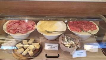 Une vitrine contenant divers produits alimentaires, notamment de la viande tranchée, du fromage et un plat de pâtes.