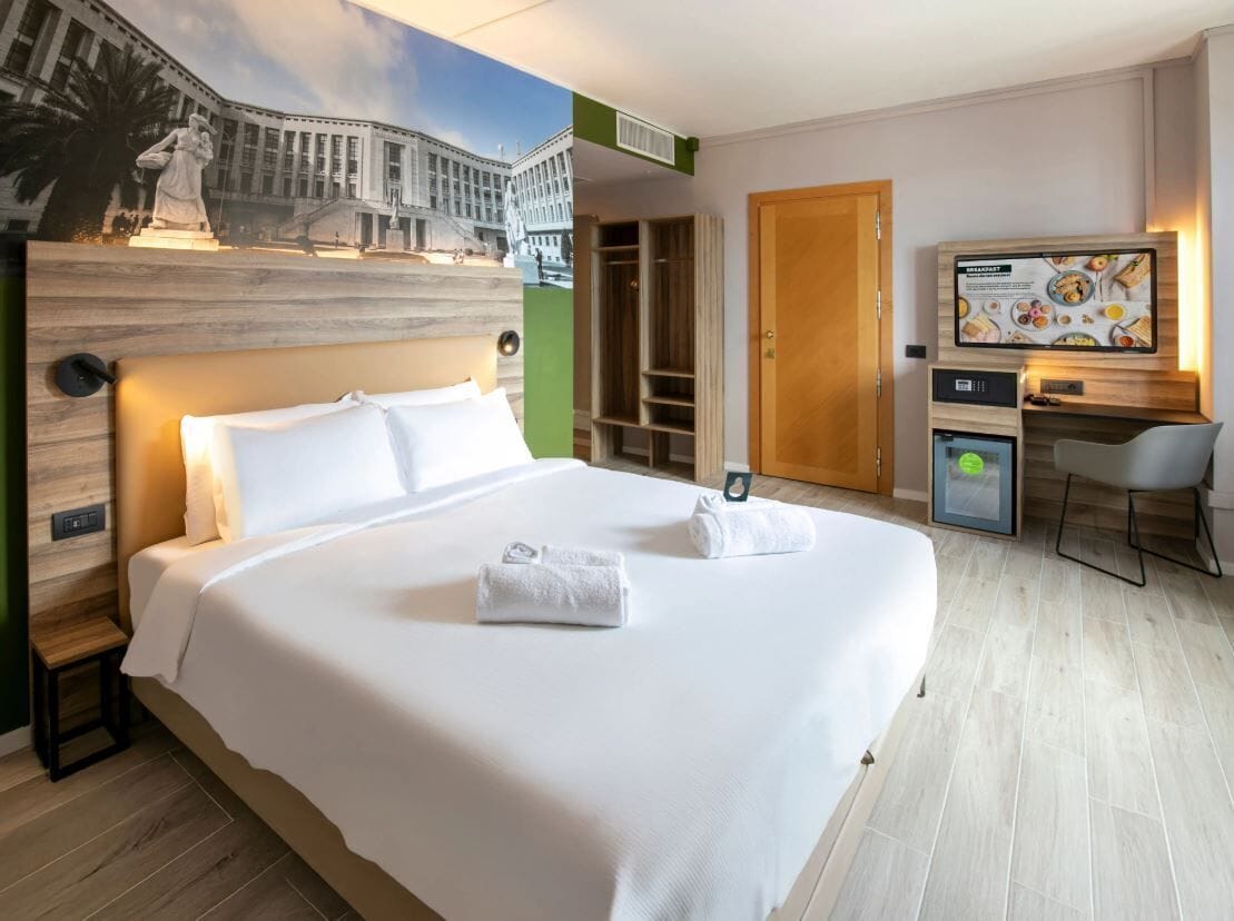 Une chambre d’hôtel avec un grand lit, un bureau, une chaise, une télévision et une fresque murale.
